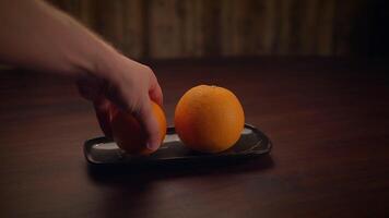 A hand placing an orange on an elegant black tray, creating a stunning visual presentation video