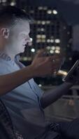 A man is immersed in using his tablet while surrounded by the vibrant night cityscape video