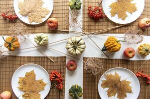 flat lay of small pumpkins and dry brown maple leafs on white plates, autumn dinner table decors photo