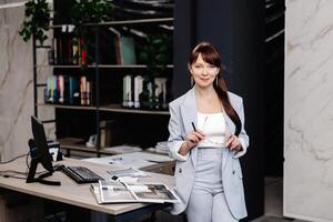 Businesswoman in a light blue suit standing near a desk with documents photo