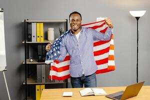 A smiling black man stands in office with an american flag backdrop in hands photo