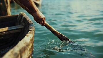 A hand grasping the oar pulls it forcefully through the water. The paddle blade is partially submerged in water, which ripples the water. photo