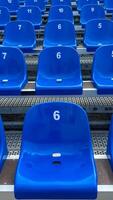 Close-up of blue plastic stadium seats, each marked with a white number. Focus on seat number 6. The organized rows create a repeating pattern, structure, and simplicity. photo