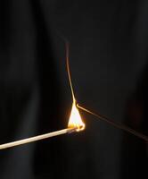 Burning match lights incense stick on black background, macro shot.long wooden match with burning head photo