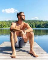 Digital detox and connecting with nature, a man relaxing on a dock by a calm lake. photo