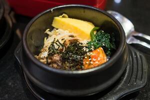 Traditional Korean Bibimbap in a Hot Stone Bowl with Fresh Vegetables, Egg, and Seaweed Garnish photo