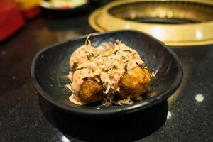 Delicious Japanese Takoyaki Balls with Toppings in a Black Bowl on a Restaurant Table photo