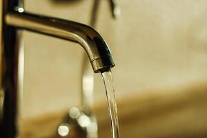 water is flowing from a chrome faucet. Plumbing in the bathroom or in the kitchen. The use of water resources. Selective focus photo