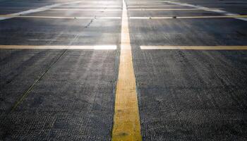 A wide, empty asphalt surface with yellow lines and a bright light in the distance. photo