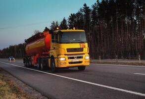 A truck carries a tank of combustible fuel on a highway against a forest and blue sky. The concept of transportation of dangerous goods on the road, license photo