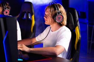 Smiling laughing pimply teen gamer in headset playing PC game at computer club with team cyber sport tournament. E-sport championship. Multiplayer online real-time strategy first-person shooter photo