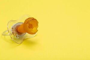 A chewed baby pacifier on a yellow background. Concept of teething in children, close-up. Copy space for text photo