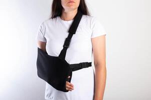 A girl on a white background with a black supporting medical bandage after a dislocation of the shoulder joint and a bone fracture. Rehabilitation after injury, orthopedics and traumatology photo