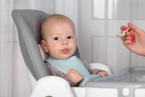 The first feeding with fruit puree for a baby boy who is 6 months old, close-up. Copy space for text photo