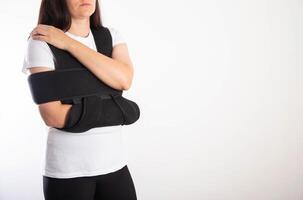 A girl in a black medical brace on the shoulder joint for rehabilitation after a fracture of the humerus and dislocation. Post-traumatic immobilization of the shoulder joint photo