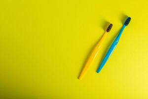 Yellow and blue toothbrush with charcoal coating on a yellow background. The concept of dental and oral hygiene in dentistry. Copy space for text, medium hard. View from above. Prevention of caries photo