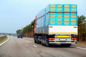 A truck with a semi-trailer transports a bulk load of insulation for construction along a country road in the spring. Copy space for text, industry photo