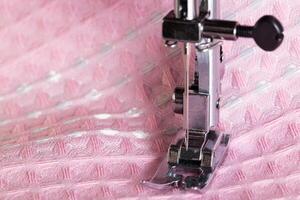 A needle with a needle holder and a sewing machine foot on a background of pink fabric. Macro, industry. Copy space for text. Tailoring services photo