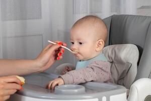 A mother feeds porridge from a spoon to a little boy who is 8 months old. Feeding infants. Copy space for text photo
