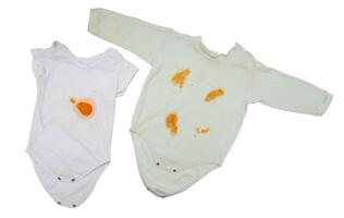 Children's clothing bodysuit with orange stains from vegetable puree on a white background, isolate. Oxygen stain remover concept, close-up photo
