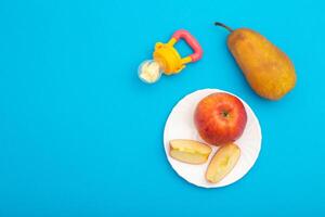 Fruits on a blue background next to a children's nibbler, close-up. Cognitive nutrition with vitamins and the development of the chewing reflex in children, close-up photo