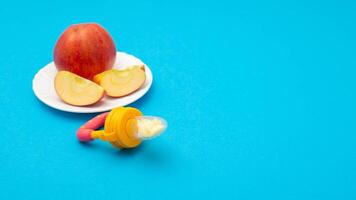 A cut apple on a plate and a baby nibbler on a blue background. The concept of feeding children fruits and vitamins. Copy space for text photo