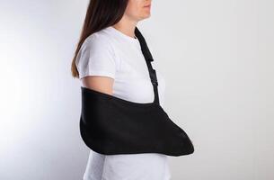 A girl in white with a fixing black bandage on her arm after an injury, a fracture of the radius and a sprain. Arm support bandage, hand immobilization photo