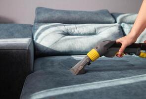 Cleaning a sofa with fabric upholstery from dirt with a professional vacuum cleaner, close-up. Copy space for text, chemical solution photo