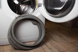 An old, torn, defective rubber hatch seal is standing near the washing machine. Spare parts replacement, industry. Copy space for text photo
