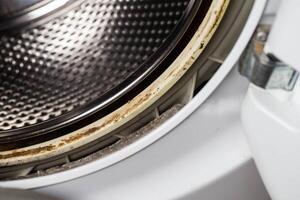 Dirt, mildew and mold in the hatch seals of the washing machine. Unsanitary and unpleasant smell. Cleaning and repairing stains in the washing machine, close-up photo