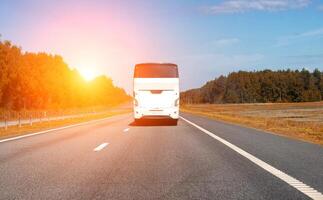 A modern comfortable passenger bus rides along the highway against the backdrop of the sun in summer. The concept of European tours by bus. Copy space for text photo