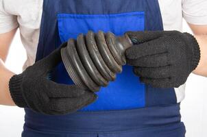 The car mechanic holds in his hands the boot of the CV joint of the car on a blue background of overalls. CV joint replacement at a car service. Close-up photo