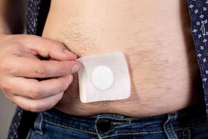 A modern medical patch for prostatitis and urinary tract infections. A man glues a urological patch on his stomach, close-up photo