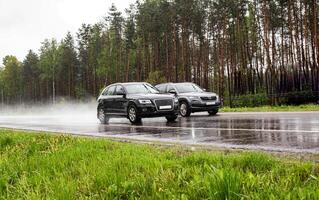 Two modern crossover cars drive on a wet country road in rainy weather against the backdrop of a forest, 4wd photo