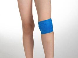 Blue elastic bandage on the knee joint on the child's leg. White background, treatment of knee pain and sprain, close-up photo