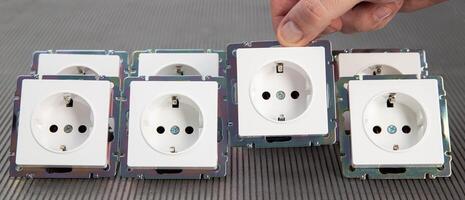 A man's hand puts an electric socket in a row. The concept of installing electrical devices. Tariffs and energy savings, close-up photo
