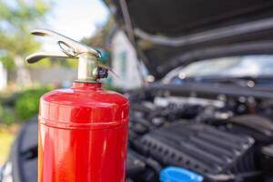 A car powder fire extinguisher is in a car with an open hood. The concept of modern fire extinguishers for extinguishing a fire in a car. Copy space for text photo