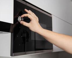 A man's hand twists a regulator button on a modern microwave oven panel. Setting the food warming timer, close-up photo