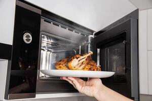 A man takes a plate of grilled chicken out of the microwave. The concept of using modern microwave ovens with grill and convection, close-up photo