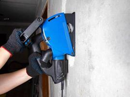 A worker in gloves works with an electric tool with a wall chaser on a reinforced concrete wall. Copy space for text photo