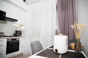 A modern humidifier sits on a table in a kitchen room. Humidification in the room, comfortable humidity and temperature photo