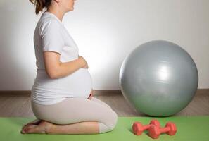 A pregnant girl goes in for sports in the 3rd trimester of pregnancy. Fitness and Pilates. Women's health. Exercises with dumbbells. photo
