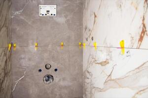 Laying modern large format tiles with the tile leveling system in the toilet. Laying tiles on the wall of the installation for the toilet. Copy space for text photo