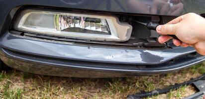 Unscrewing and disassembling the fog lamp in a car to replace the light bulb with a new one, close-up photo