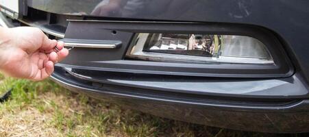 a car mechanic removes a fog lamp from a passenger car to replace a light bulb, close-up photo