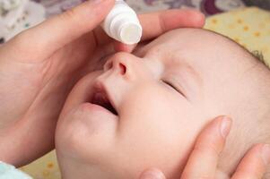 A mother instills medicinal drops in the child's eye to treat pus and tears. Eye drops with vitamins, close-up photo