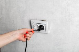 The girl incorrectly removes the electric plug from the socket and breaks the socket. Danger of electric shock, close-up. Copy space for text photo