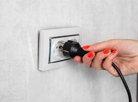 The girl removes the electrical plug from the socket and breaks the socket out of the socket. Incorrect removal of the electrical plug. Risk of electric shock, close-up photo