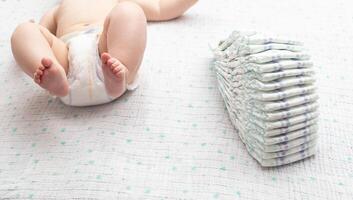 A little caucasian baby boy in a diaper lies on a white background and plays with a bunch of diapers. Copy space for text photo