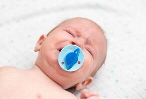 Little baby boy crying with a pacifier in his mouth. The concept of weaning the habit of sucking a pacifier in children, close-up. Copy space for text photo